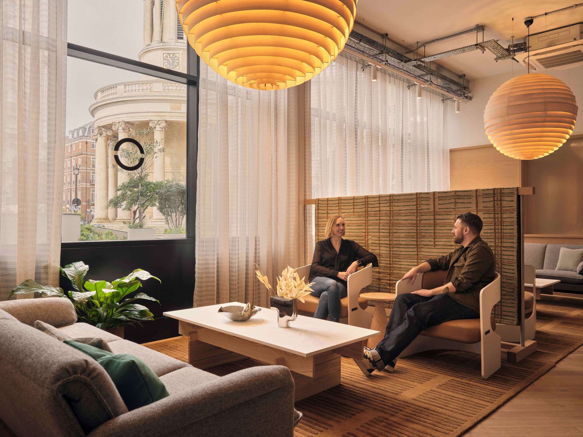 Warm-toned lounge with textured pendant lights and city views through sheer curtains at Henry Wood House.